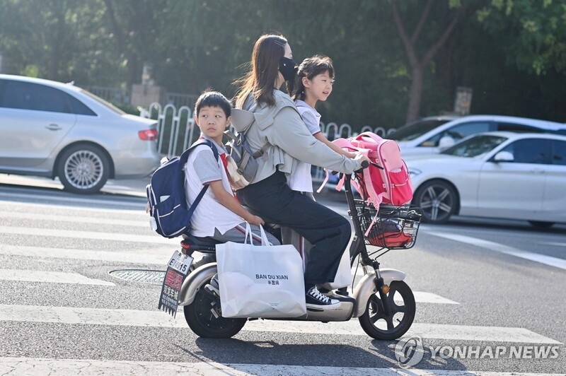 중국 베이징에서 지난 1일 한 여성이 전동 스쿠터에 두 초등학생을 태우고 가는 모습. / 사진 = 연합뉴스