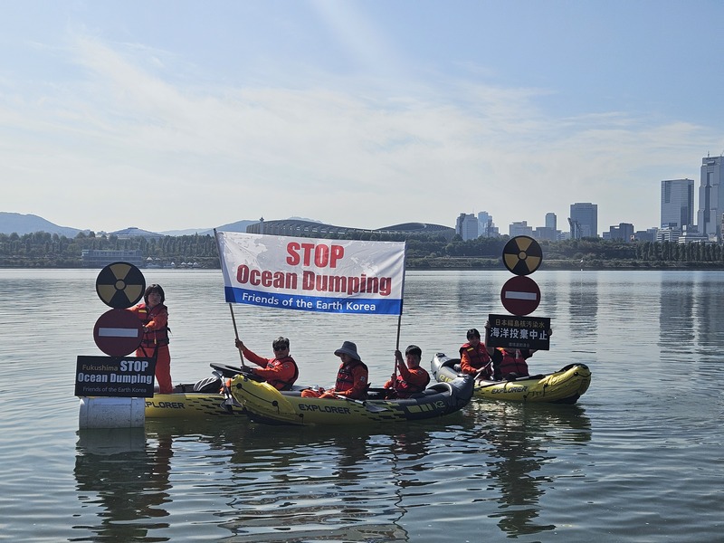 카약 위에서 해양 투기 반대 문구가 영어로 적힌 현수막을 들고 있는 환경단체들
